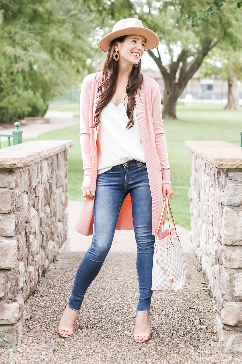 Casual Pink Cardigan Outfit styled by popular affordable fashion style blogger Stephanie Ziajka on Diary of a Debutante, Amazon light pink cardigan styled with J.Crew Factory scalloped cami top, AG the Legging super skinny jeans, Amazon Lanzom wide brim wool fedora hat, Amazon Louis Vuitton Neverfull dupe bag, Amazon nude block heel sandals, Amazon rattan earrings, and Amazon gold circle pendant necklace by Stephanie Ziajka on Diary of a Debutante